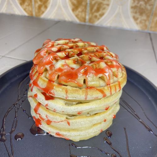 A stack of waffles drizzled with strawberry and chocolate sauce