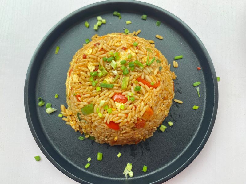 A dome of egg fried rice topped with chopped spring onions, plated on a dark plate